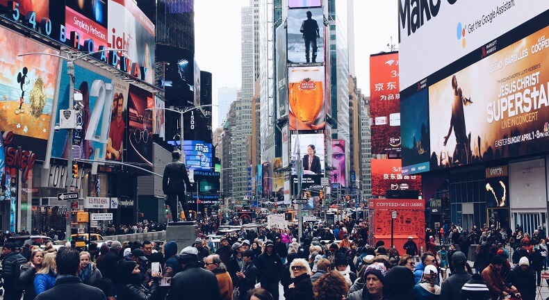 A crowd of people walking on the street. Above and around are digital billboards. Programmatic digital out of home sales would make it much more efficient to sell inventory on these screens.