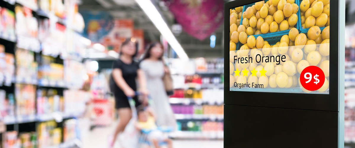 A digital signboard in a grocery store. It is displaying dynamic DOOH content that advertises the price of oranges.