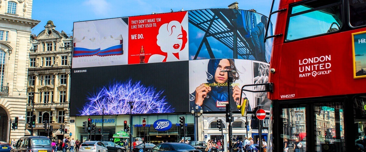 Out-of-home advertising displaying on a huge digital display at Piccadilly Circus in London, England. Ads for Coca Cola, Samsung, and other prominent brands are present on the screen.