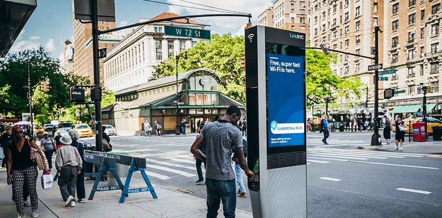 A man standing at a LinkNYC kiosk on a sunny day.