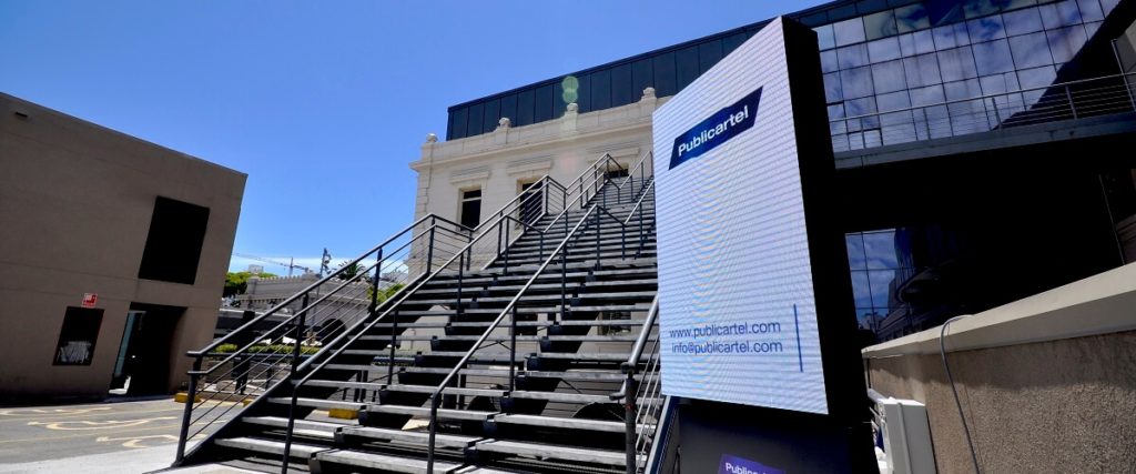 The Publicartel logo playing on a Publicartel screen in front of a building.