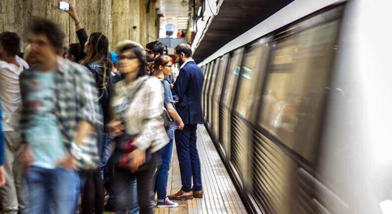 A businessman in a suit and leather shoes standing out from the crowd on a subway platform. With programmatic DOOH, it's easier to target specific demographics like his for an ad campaign.