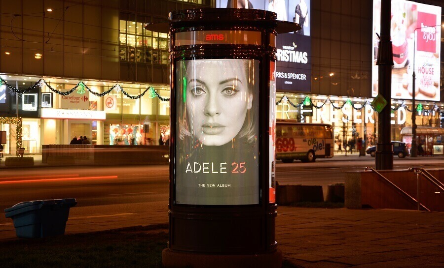 A digital poster in Warsaw, Poland. It is on the side of the street at nighttime, and displays an ad for the Adele album "25."