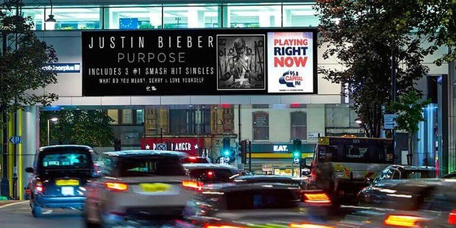 A long digital screen over a street. On display is an ad for Justin Bieber's album "Purpose," and a note saying that it was playing at that moment on 95.8 Capital FM.