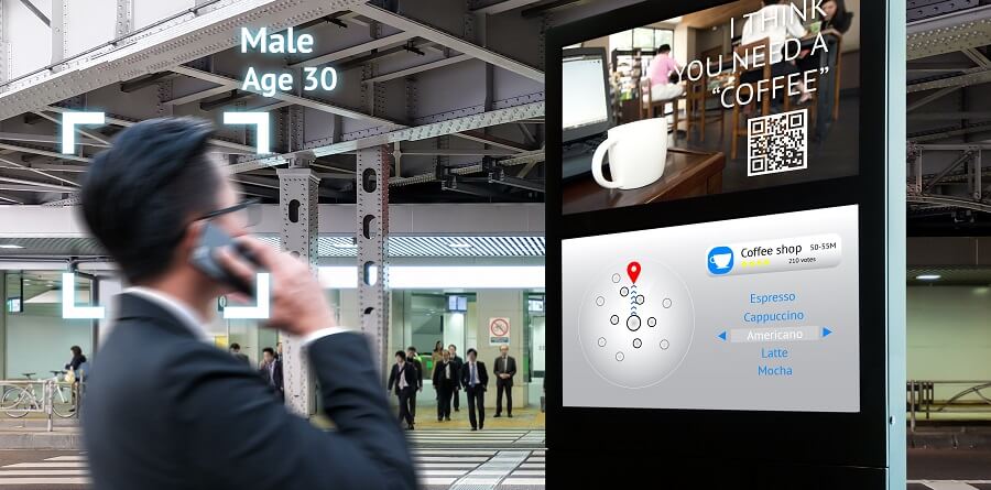 A man looking at a digital sign in a public space. Text superimposed on the image suggests that facial recognition software has recognized the man is a man, aged 30, and that this has triggered an ad for coffee.